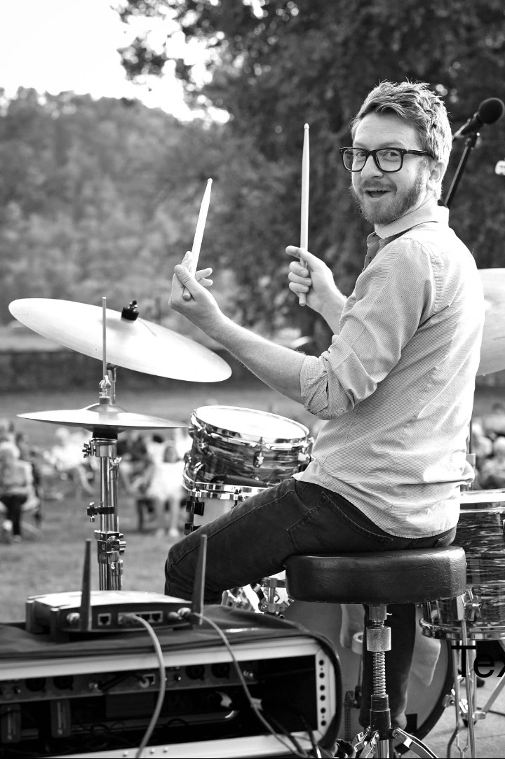 a headshot of Zack Kennedy holding drumsticks and sitting at a drum set